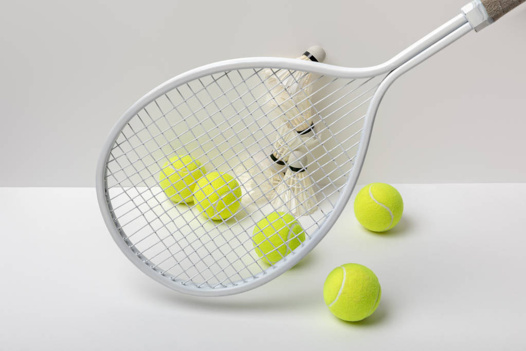 білі бадмінтонні човники та яскраво-жовті тенісні м'ячі біля ракетки на білому тлі
 - Фото, зображення