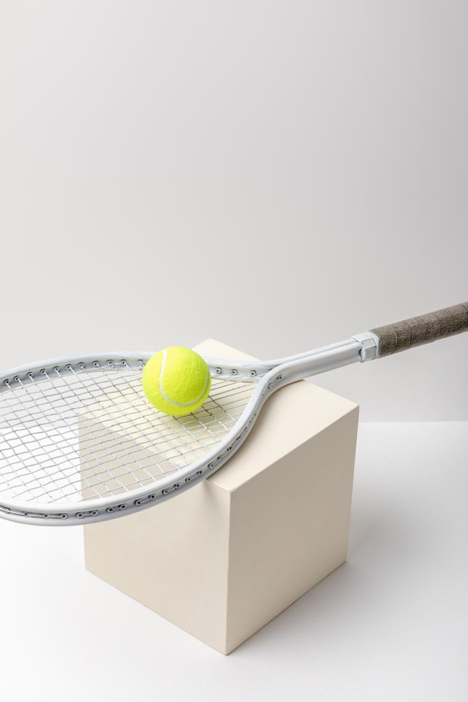 felgele tennisbal met racket op kubus op witte achtergrond - Foto, afbeelding