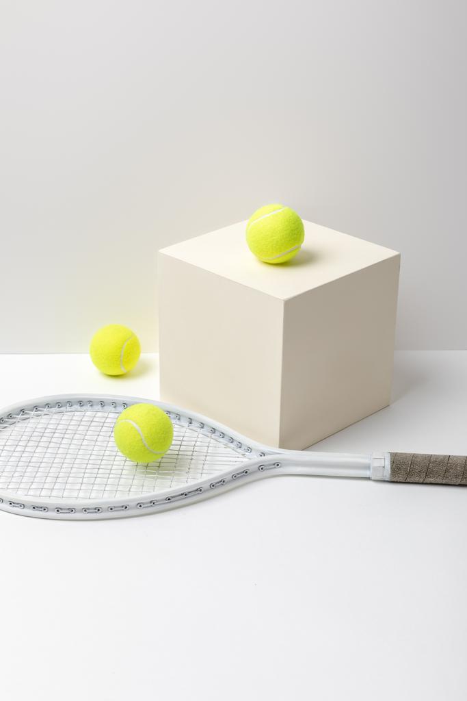 ρακέτα του τένις και φωτεινές κίτρινες μπάλες του τένις στον κύβο σε λευκό φόντο - Φωτογραφία, εικόνα