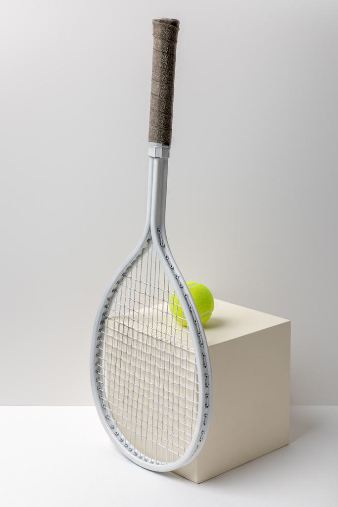 Tennisschläger und knallgelber Tennisball auf Würfel auf weißem Hintergrund - Foto, Bild