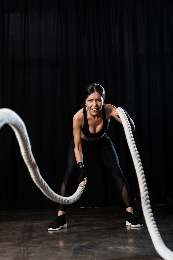 selectieve focus van Sportvrouw trainen met Battle touwen op zwart  - Foto, afbeelding