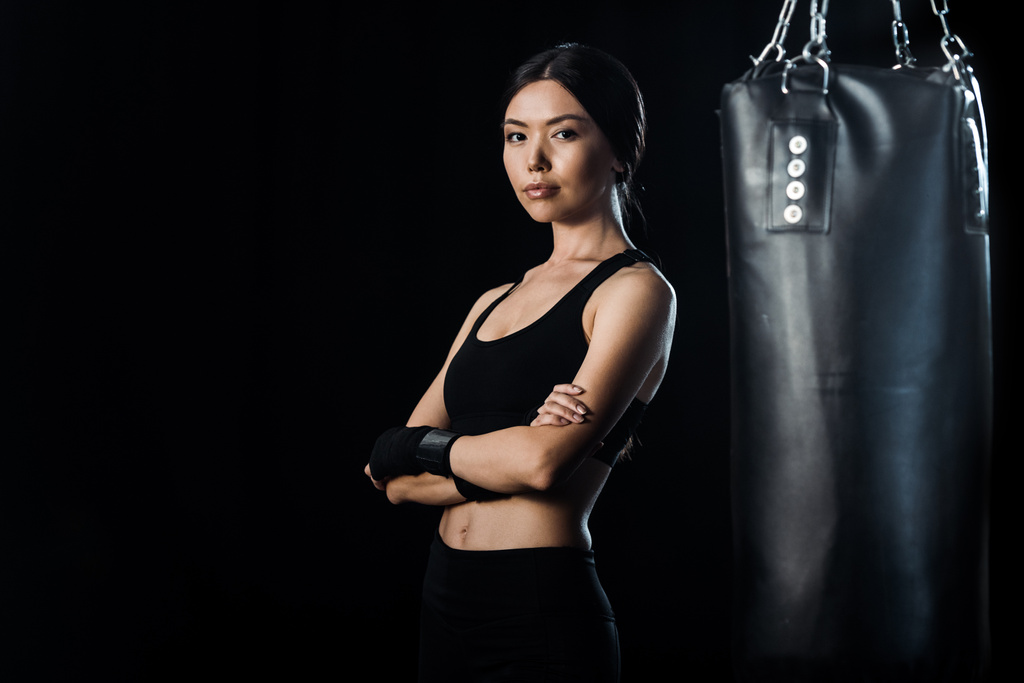 селективное внимание привлекательной девушки, стоящей с обрезанными руками рядом с боксерской грушей, изолированной на черном
  - Фото, изображение
