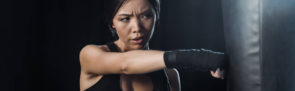 панорамный снимок девушки, работающей рядом с боксерской грушей, изолированной на черном
  - Фото, изображение