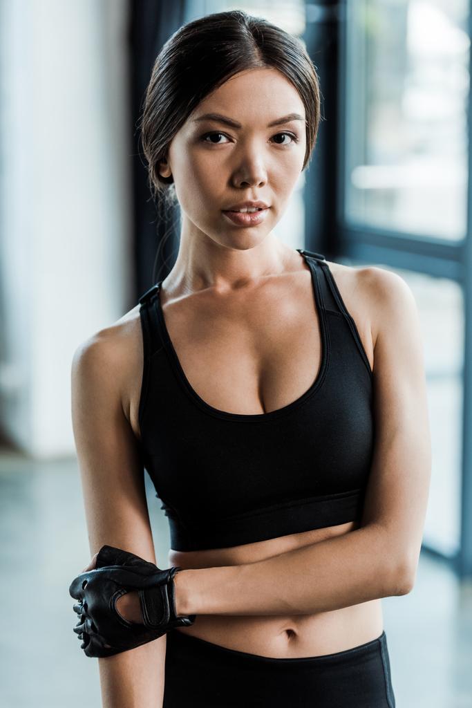 atrakcyjna kobieta w odzieży sportowej patrząc na kamerę w siłowni  - Zdjęcie, obraz