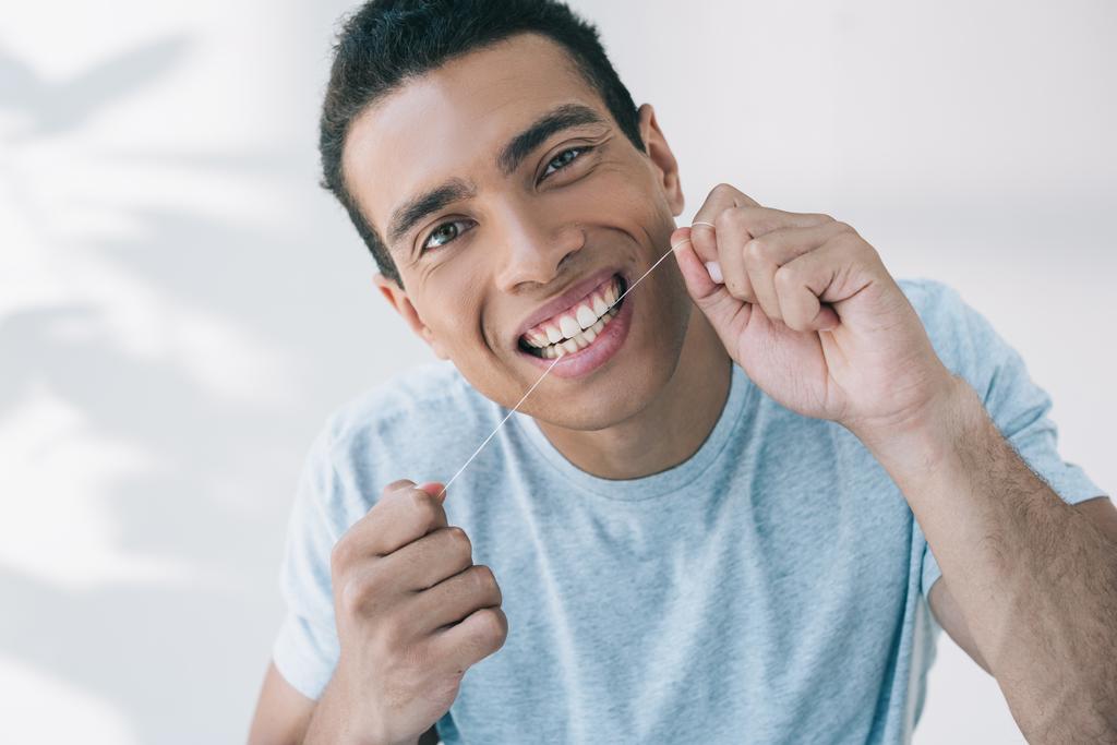 молодой человек, пользующийся зубной нитью и смотрящий в камеру
 - Фото, изображение