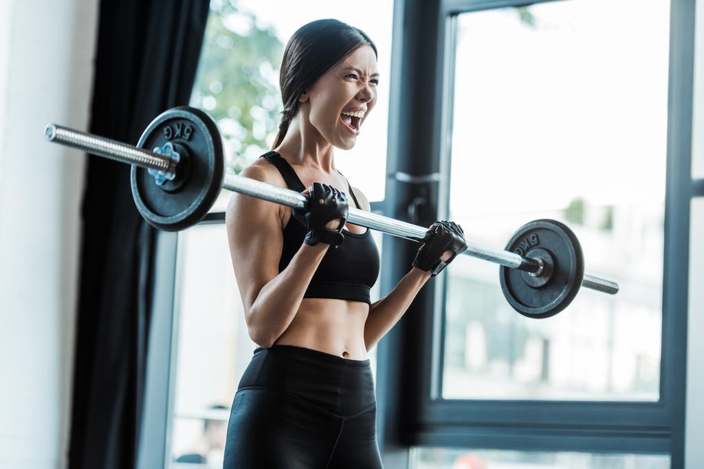  emotionele jonge vrouw in Sportswear trainen met barbell in Gym  - Foto, afbeelding