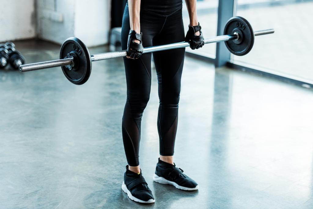 vista recortada de mujer joven en ropa deportiva haciendo ejercicio con barra en el gimnasio
  - Foto, imagen