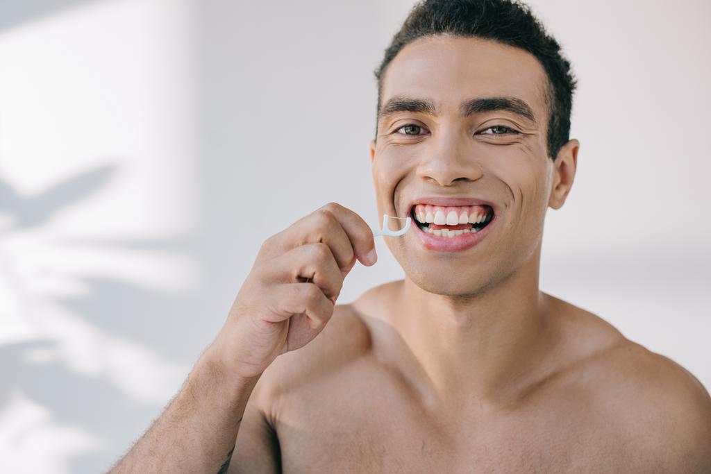 retrato de hombre de raza mixta guapo usando hilo dental en palo y mirando a la cámara
 - Foto, Imagen
