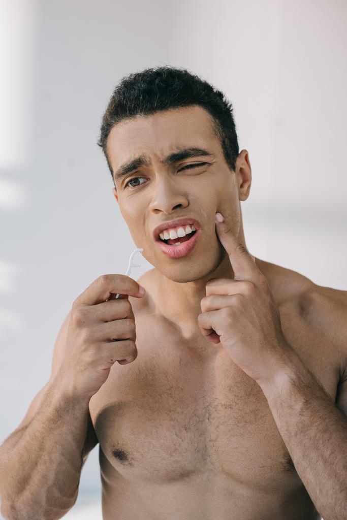 knappe man met tandpijn vasthouden tandheelkundige floss op stok en op zoek weg - Foto, afbeelding