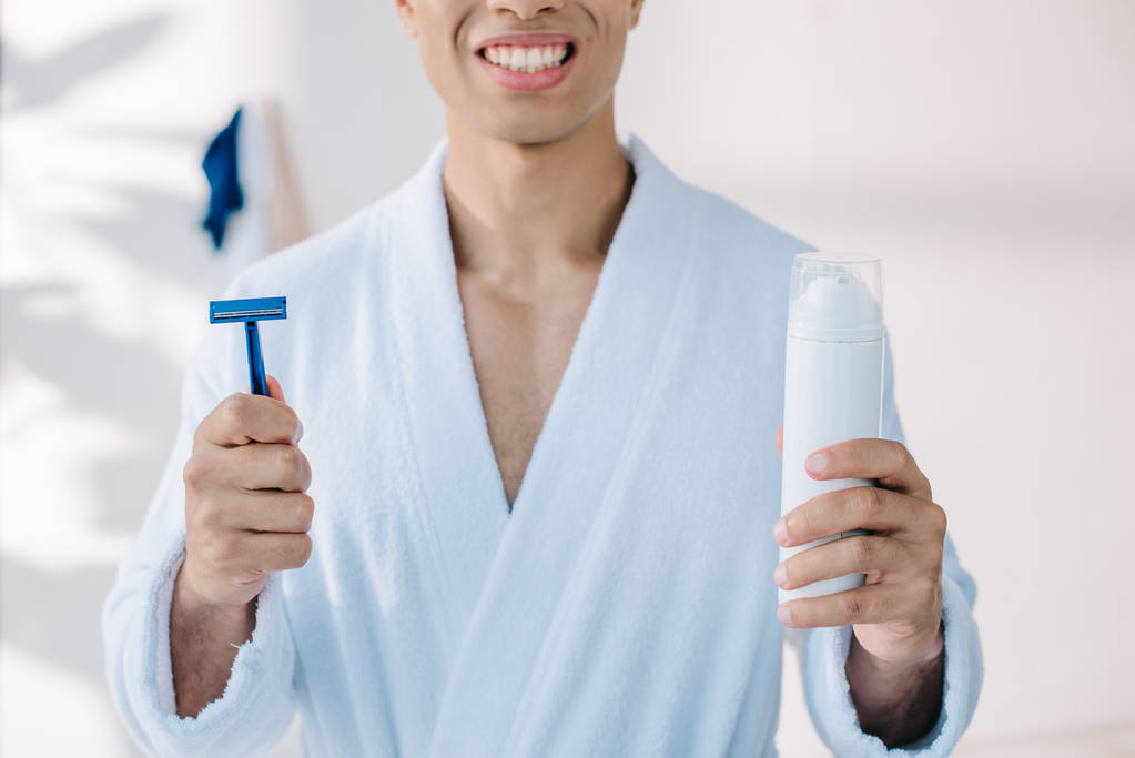 abgeschnittene Ansicht eines Mannes im Bademantel mit Rasiermesser und Spender mit Rasierschaum - Foto, Bild