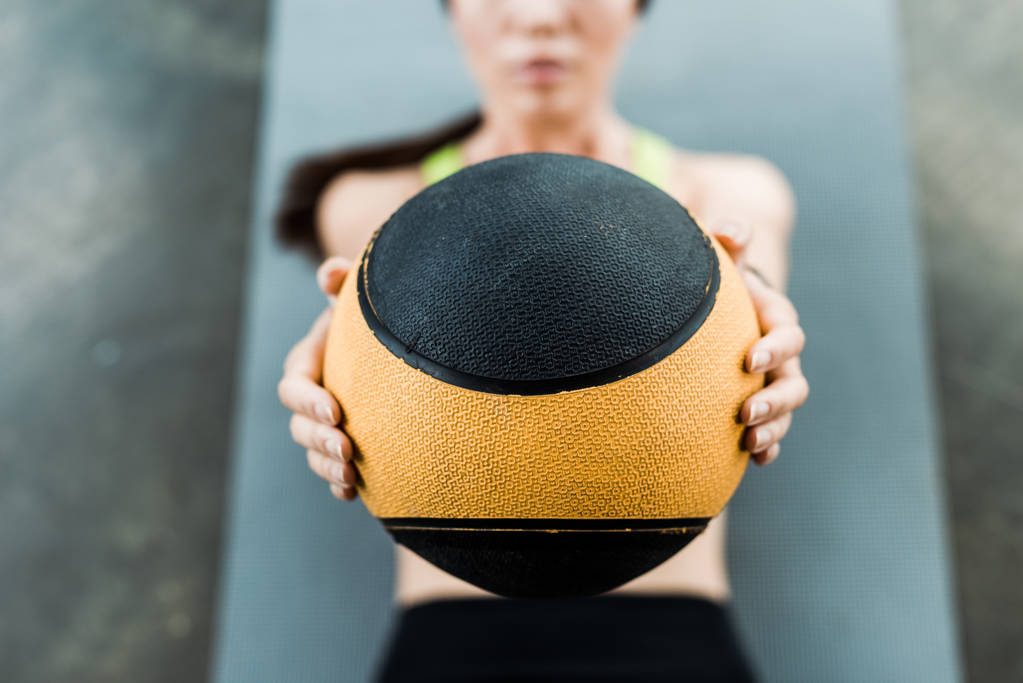 επιλεκτική εστίαση της γυναίκας κρατώντας μπάλα, ενώ βρίσκεται σε χαλάκι γυμναστικής  - Φωτογραφία, εικόνα