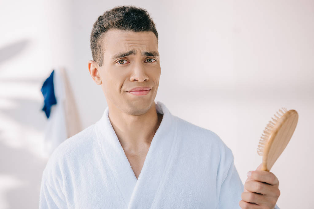 disappointed young man in bathrobe holding hairbrush, looking at camera and making grimace - Photo, Image