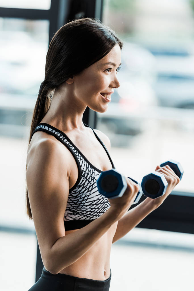 mujer positiva y deportiva sosteniendo pesas en el gimnasio
  - Foto, imagen