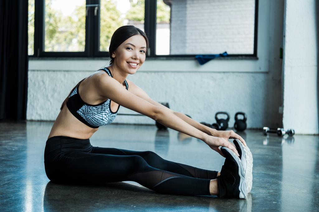 young sportswoman stretching and smiling in gym - Photo, Image