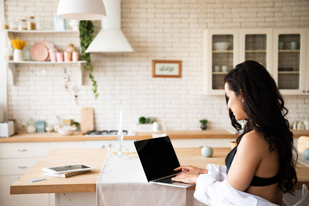 vue arrière de fille sexy en sous-vêtements noirs et chemise blanche en utilisant un ordinateur portable tout en étant assis dans la cuisine
 - Photo, image