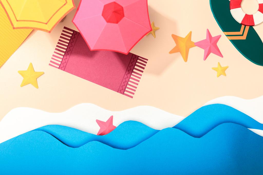 верхний вид бумажного пляжа с морскими звездами, полотенцами, зонтиками и доской для серфинга с спасательным буем на песке у моря
 - Фото, изображение