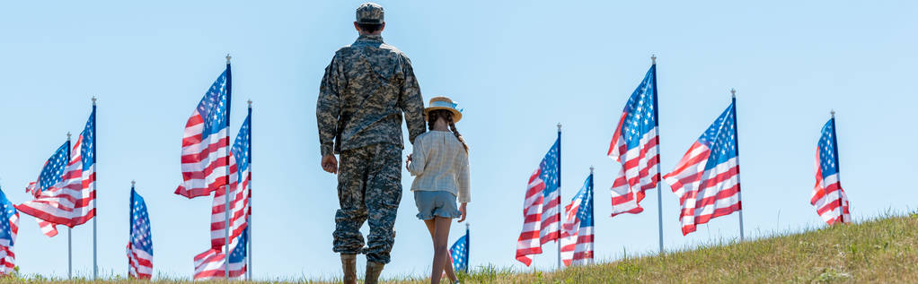 panoramic shot of father in military uniform holding hands with daughter near american flags  - Photo, Image
