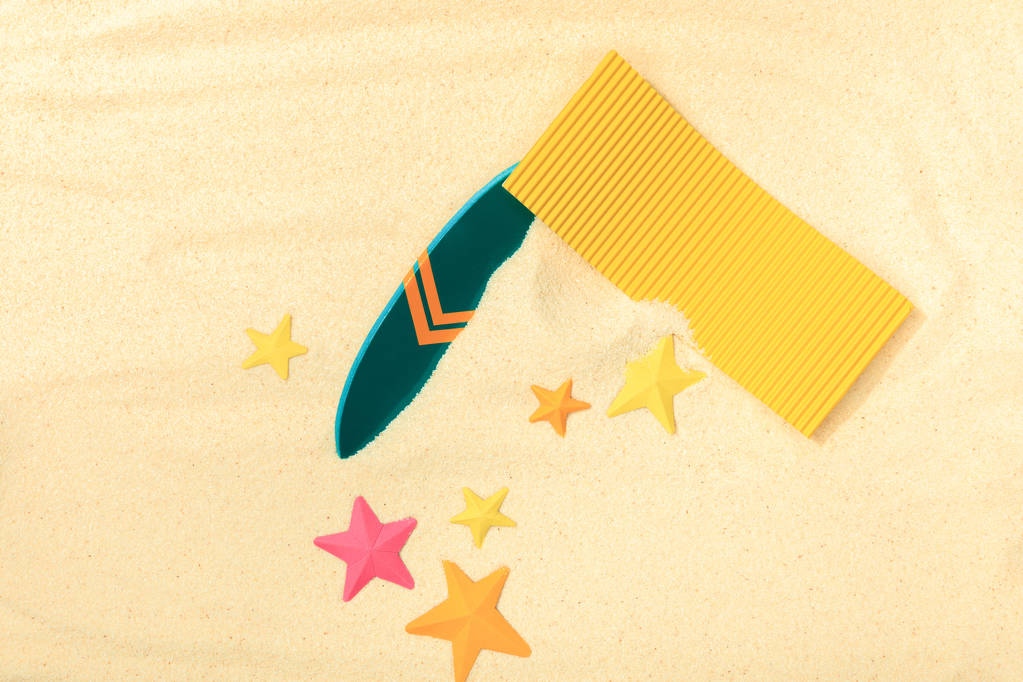 vista superior da praia de papel com prancha verde, toalha amarela e estrelas-do-mar em areia texturizada
  - Foto, Imagem