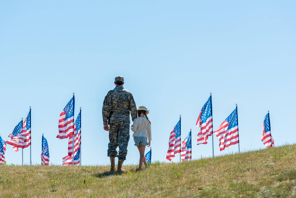 back view of father in military uniform holding hands with kid near american flags  - Photo, Image
