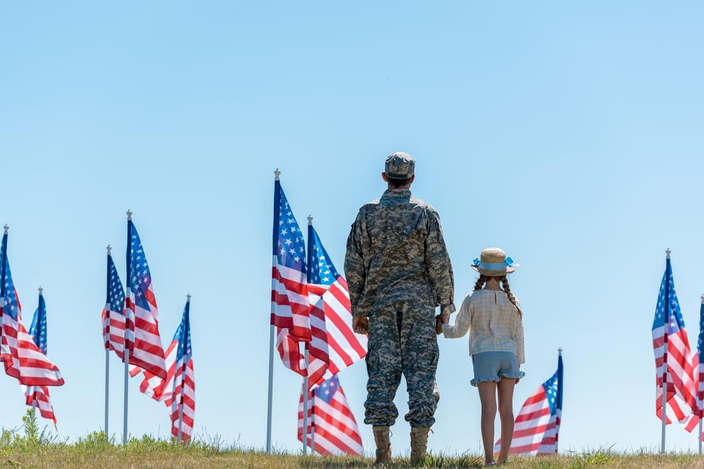 back view of father in military uniform holding hands with child near american flags  - Photo, Image