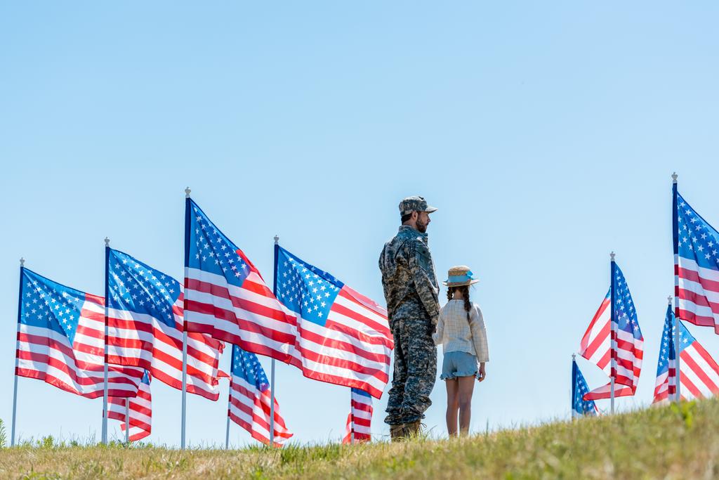 アメリカの旗の近くに娘と一緒に立っている軍服の男  - 写真・画像