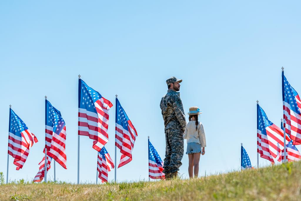 アメリカの旗の近くに娘と一緒に立っている制服を着た軍人  - 写真・画像