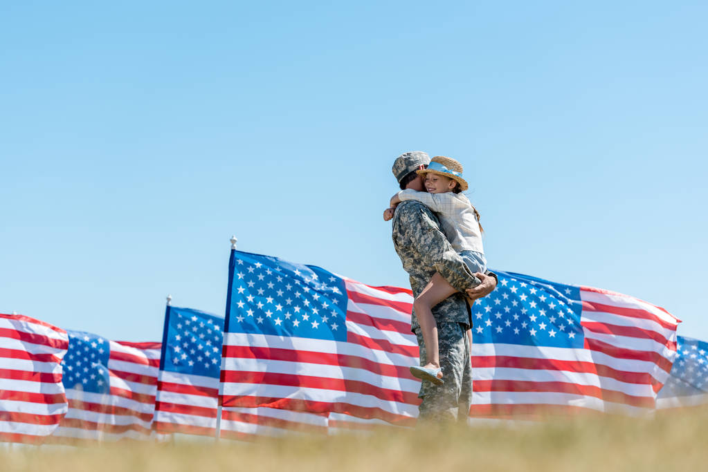 Amerikan bayrakları yakınında silah neşeli çocuk tutan askeri adamın seçici odak  - Fotoğraf, Görsel