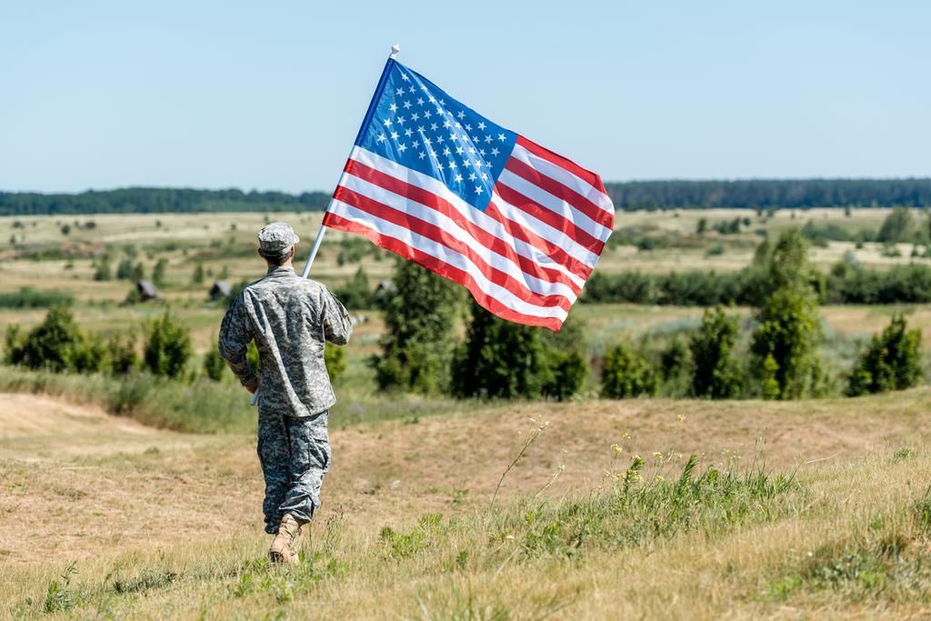 制服姿の軍人が草の上を歩き、アメリカ国旗を掲げる  - 写真・画像