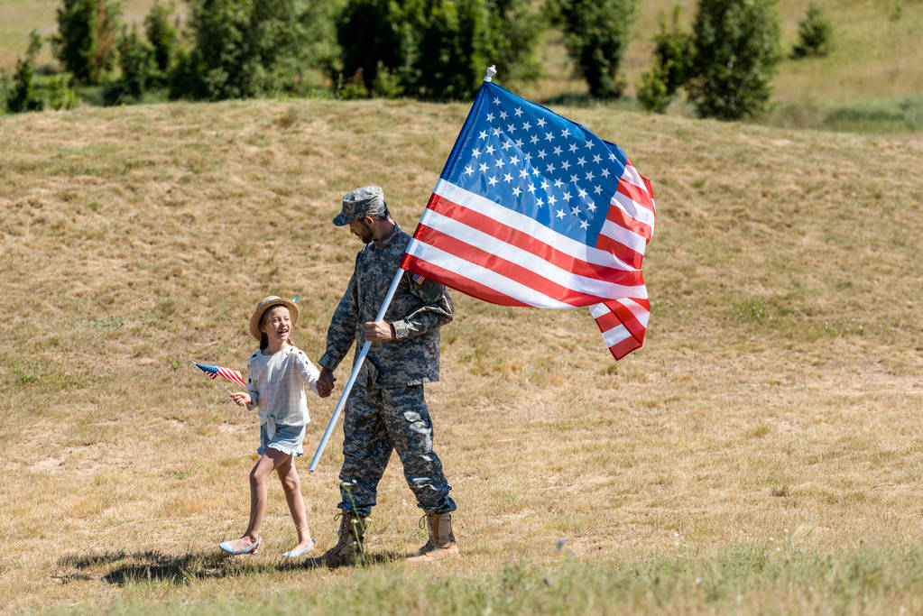 στρατιωτικός και ευτυχισμένο πατριωτικό παιδί κρατώντας τα χέρια και τις αμερικανικές σημαίες  - Φωτογραφία, εικόνα