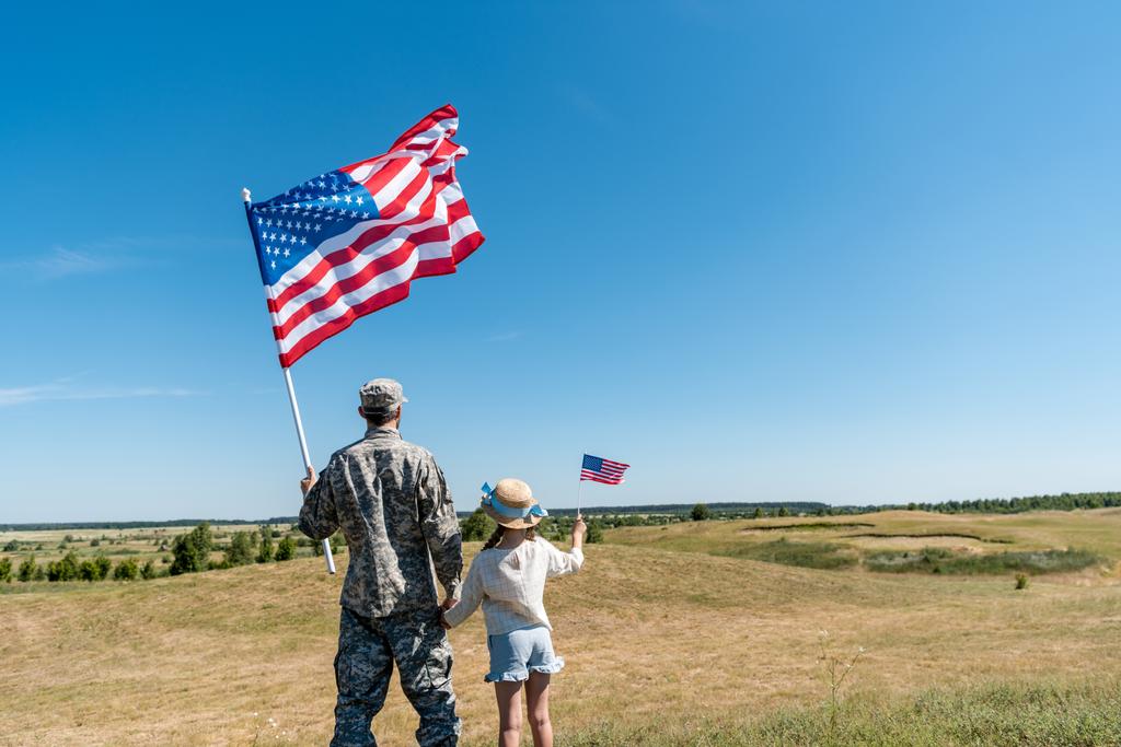 Hátulnézet a katonai apa és hazafias gyerek tartja az amerikai zászlók  - Fotó, kép