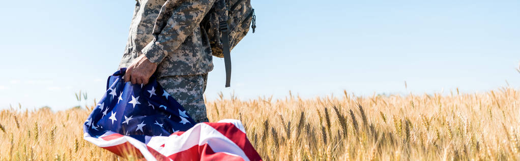 askeri üniformalı vatansever askerin sahada dururken Amerikan bayrağı tutan panoramik görüntüsü  - Fotoğraf, Görsel