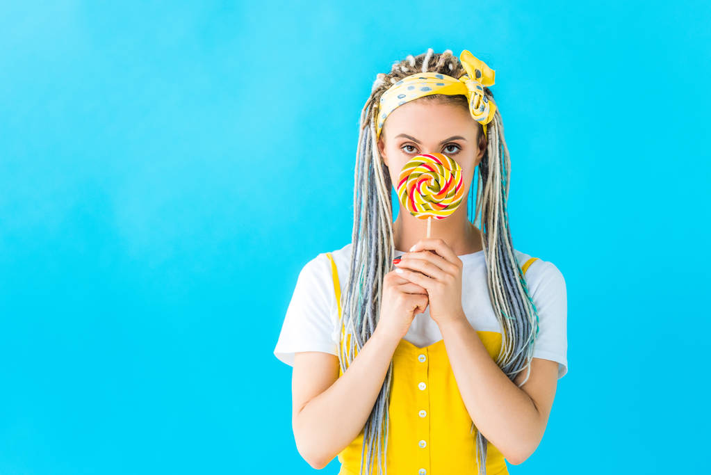 mooi meisje met dreadlocks bedekt gezicht met Lollipop geïsoleerd op Turquoise - Foto, afbeelding