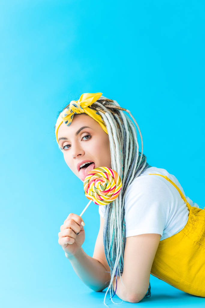 girl with dreadlocks licking lollipop on turquoise - Photo, Image
