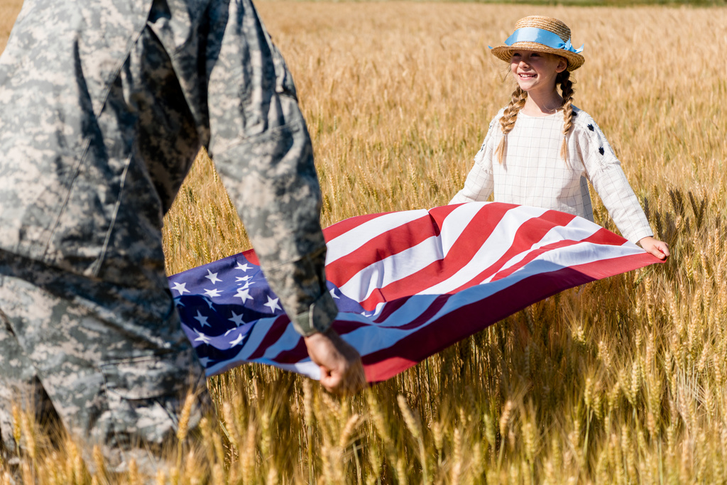 abgeschnittene Ansicht eines Mannes in Militäruniform mit amerikanischer Flagge und niedlicher Tochter im Feld  - Foto, Bild