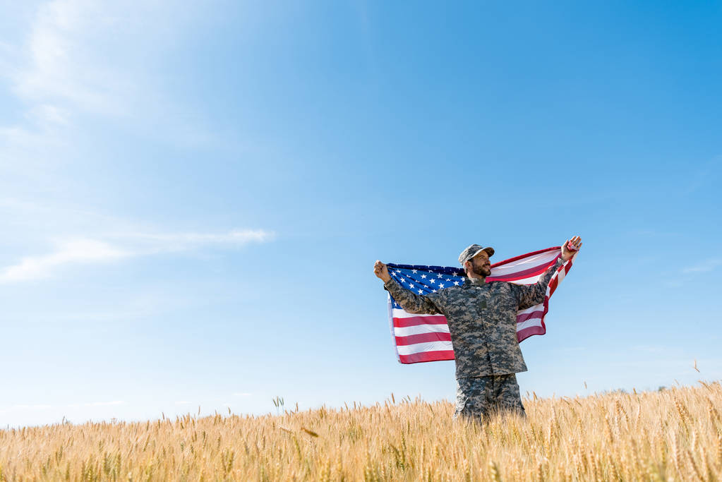 soldier in cap and military uniform holding american flag in field  - Photo, Image