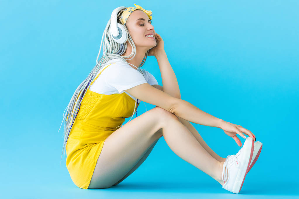 smiling girl with dreadlocks in headphones sitting on turquoise - Photo, Image