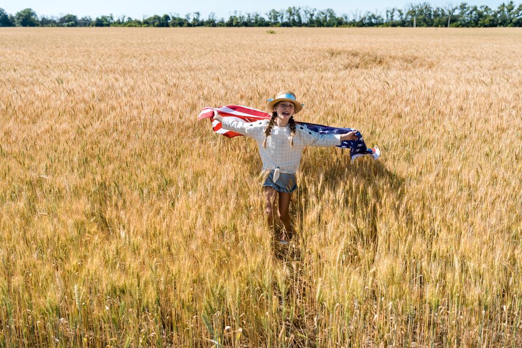 cute and cheerful kid holding american flag with stars and stripes in golden field  - Photo, Image