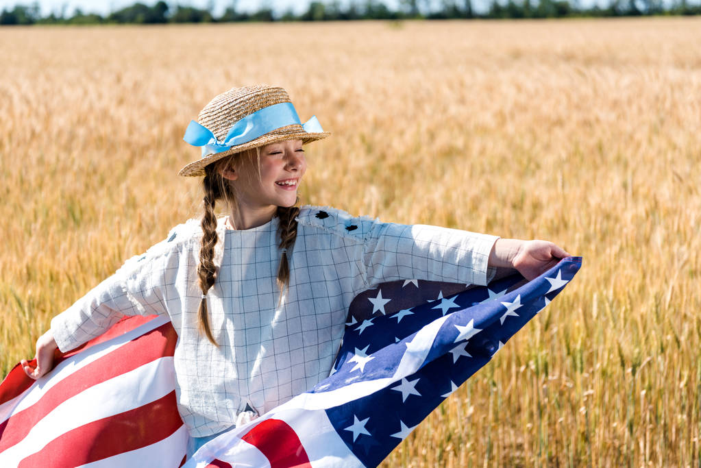黄金のフィールドで星とストライプでアメリカの旗を保持する陽気な子供  - 写真・画像