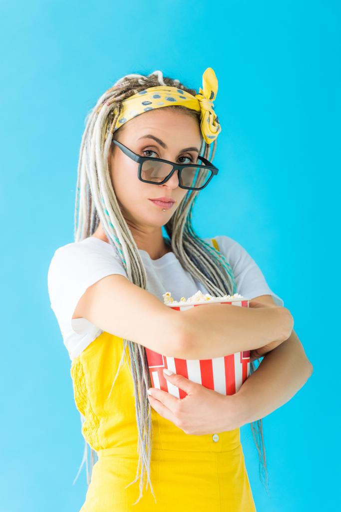 girl with dreadlocks in 3d glasses holding popcorn isolated on turquoise and looking at camera - Photo, Image
