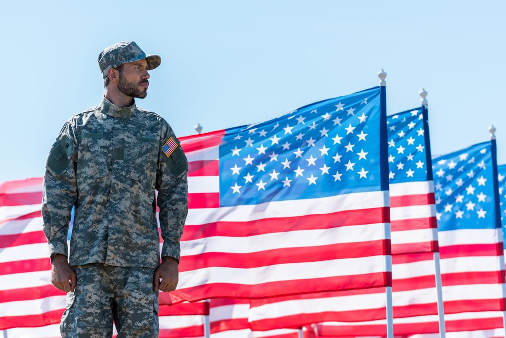 青空に対してアメリカの旗の近くに立つ制服を着た兵士  - 写真・画像