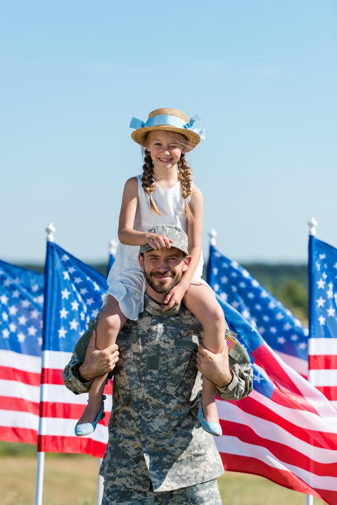 amerikan bayrakları yakınında hasır şapka lı neşeli kızı omuzlarında tutan yakışıklı adam  - Fotoğraf, Görsel