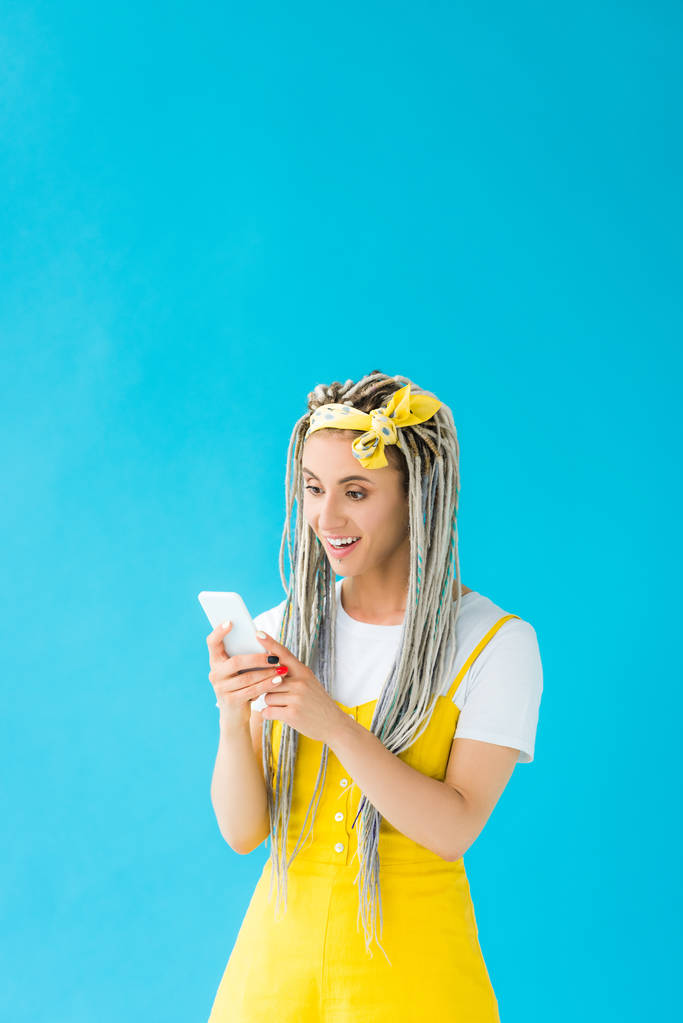 happy girl with dreadlocks using smartphone isolated on turquoise - Photo, Image