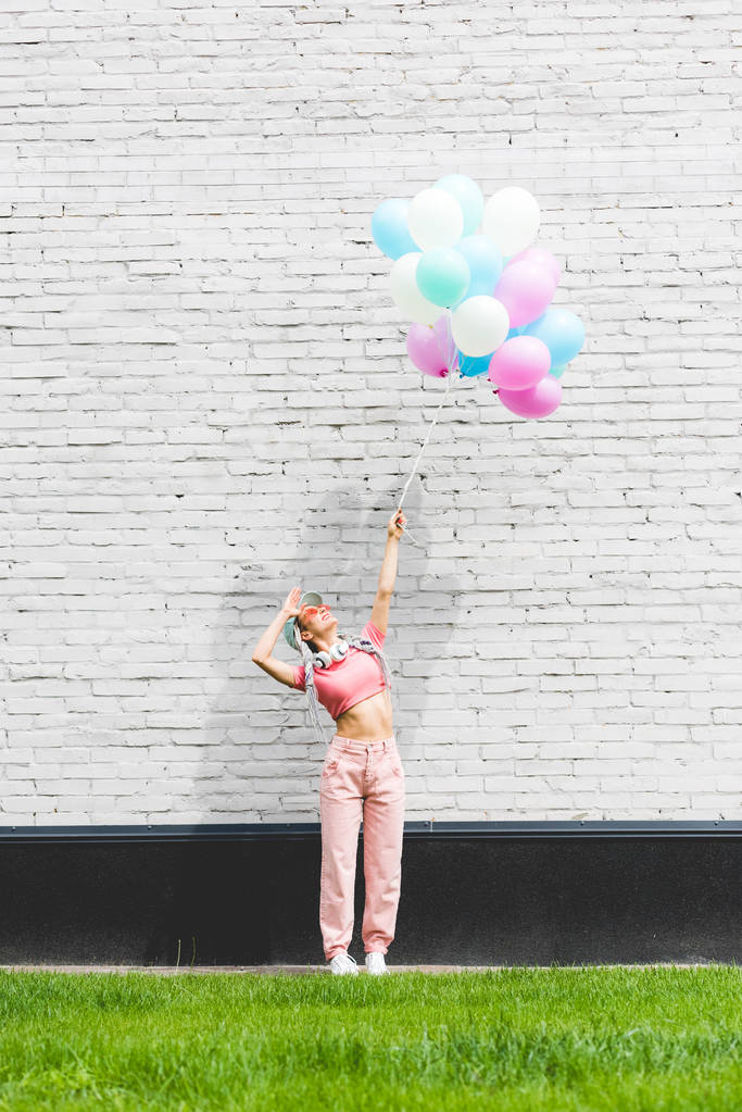 κομψό κορίτσι που ποζάρει με διακοσμητικά μπαλόνια κοντά σε τοίχο τούβλο - Φωτογραφία, εικόνα