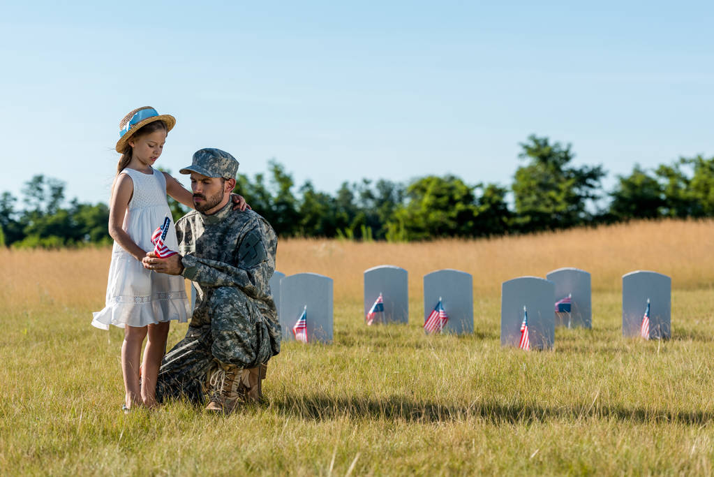 militar homem de uniforme sentado perto da criança e lápides no cemitério
  - Foto, Imagem