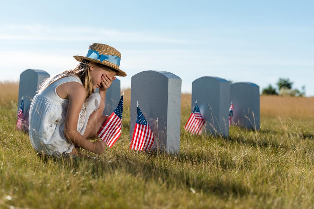 lapsi olki hattu kattaa kasvot istuessaan lähellä hautakiviä Amerikan liput
  - Valokuva, kuva