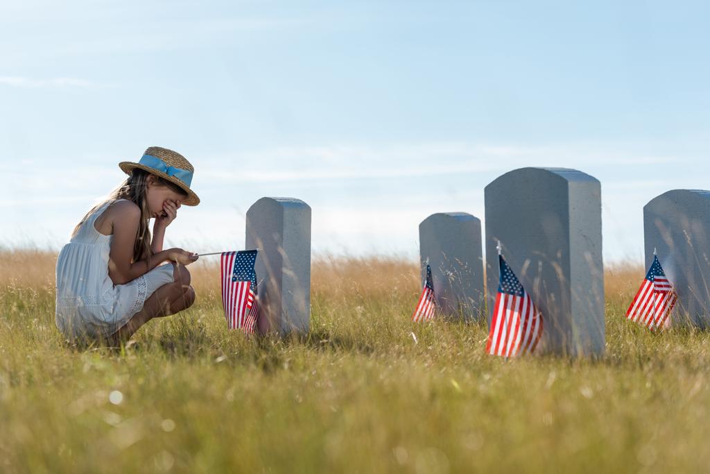 foyer sélectif de l'enfant couvrant le visage tout en étant assis près des pierres tombales avec des drapeaux américains
  - Photo, image