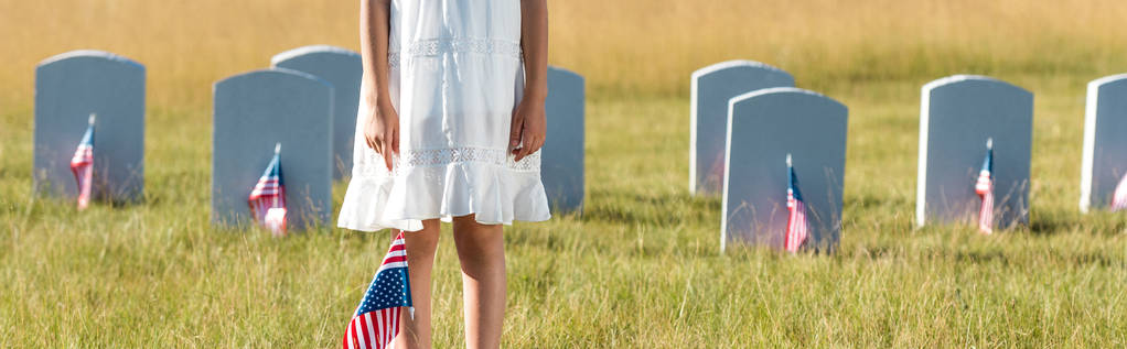 panoramic shot of kid in white dress standing on graveyard with american flag  - Photo, Image