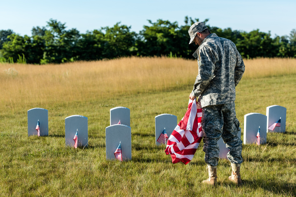 military man in uniform holding american flag in graveyard  - Photo, Image
