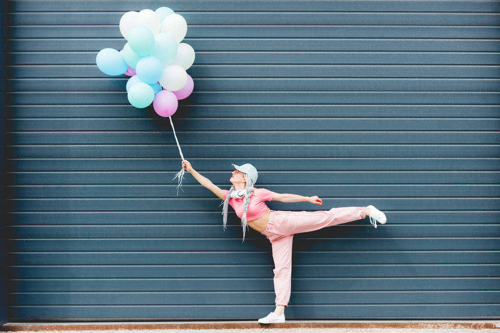 κομψό κορίτσι που ποζάρει με διακοσμητικά μπαλόνια κοντά στον τοίχο - Φωτογραφία, εικόνα