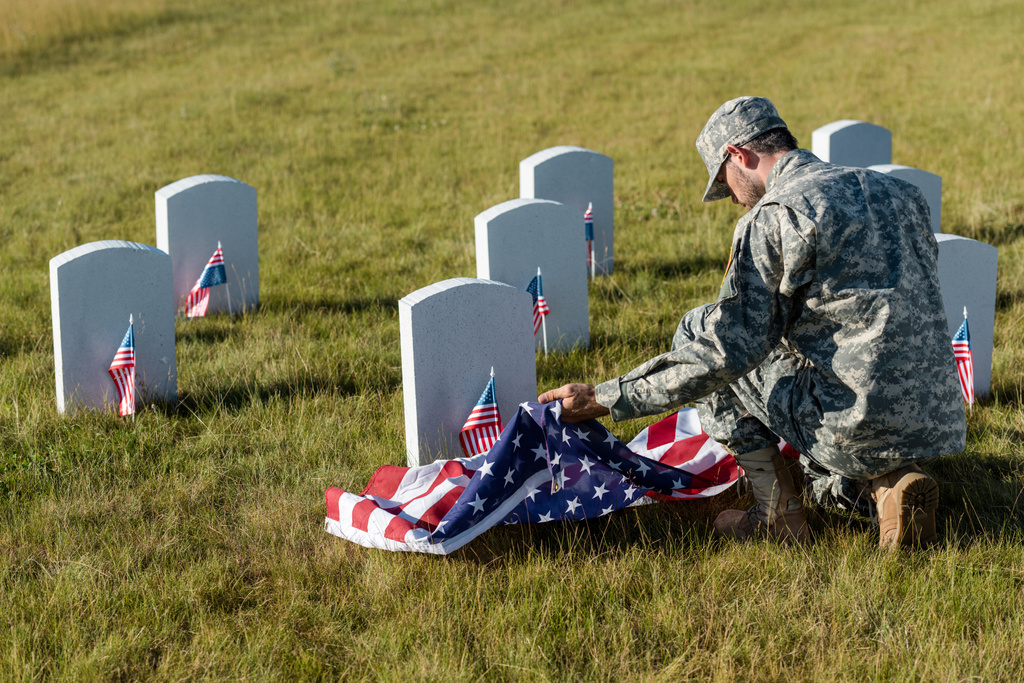 Soldat in Tarnuniform und Mütze mit amerikanischer Flagge auf dem Friedhof  - Foto, Bild